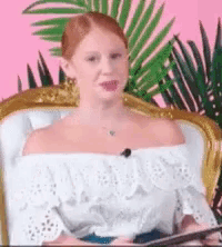 a woman in a white off the shoulder top is sitting in a chair with a palm tree in the background .
