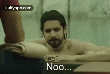 a shirtless man with a beard is laying in a pool with a person standing behind him .