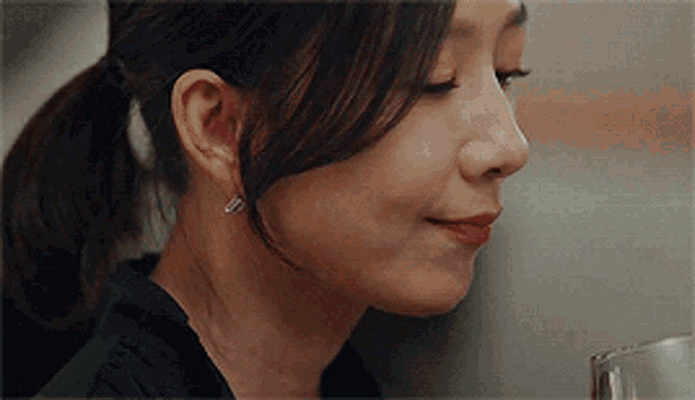 a close up of a woman 's face with a ponytail and a glass in her hand .