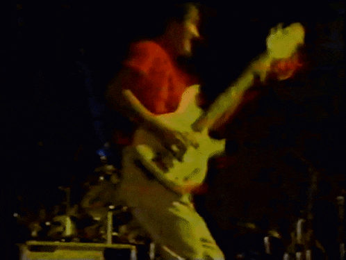 a man in a red shirt is playing a white guitar on a stage .