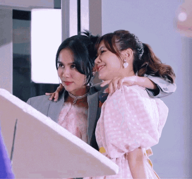 a woman in a pink dress is hugging another woman in a grey jacket