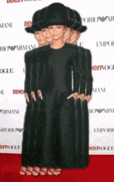 a woman in a black dress and hat is standing on a red carpet in front of a wall that says emporio armani