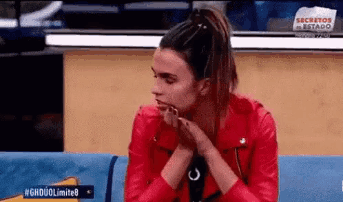 a woman in a red leather jacket is sitting on a blue couch with her hands on her face .