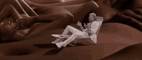 a man in a white suit is sitting in a chair in front of a group of naked women .