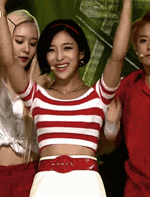 a woman in a red and white striped crop top stands with her arms in the air