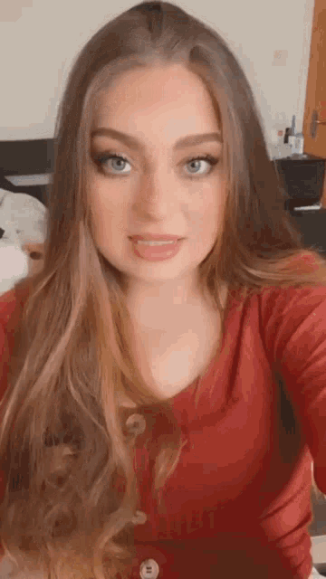 a woman with long hair and blue eyes is taking a selfie in a bedroom .