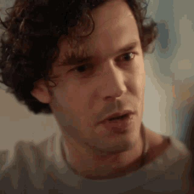 a close up of a man 's face with curly hair wearing a gray shirt .