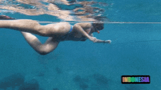 a woman in a bikini is swimming in the ocean with indonesia written in the corner