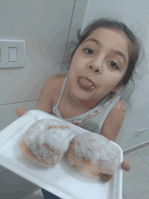 a little girl sticks her tongue out while holding a tray of donuts