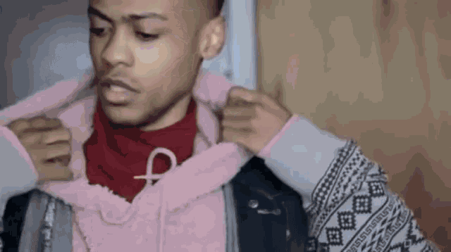 a man wearing a pink hoodie and a red turtleneck is being helped by another man .