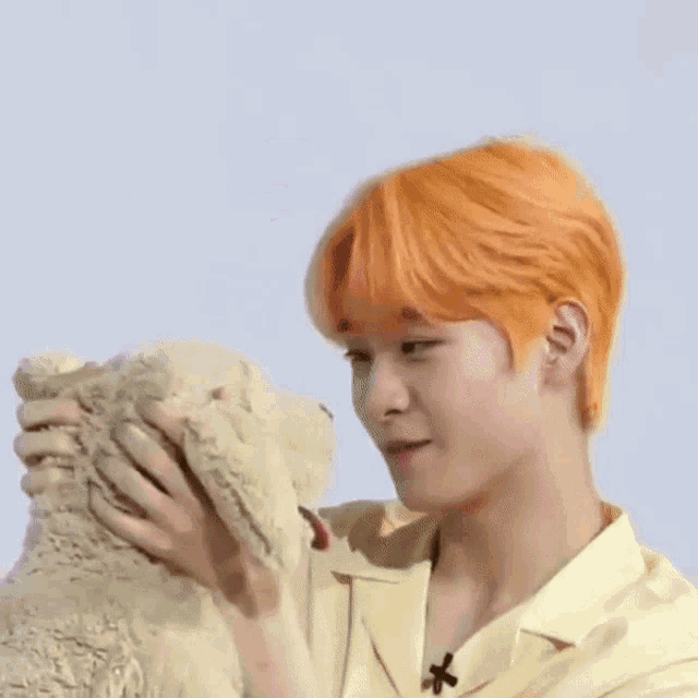 a man with orange hair is petting a teddy bear with a pink heart in his head .