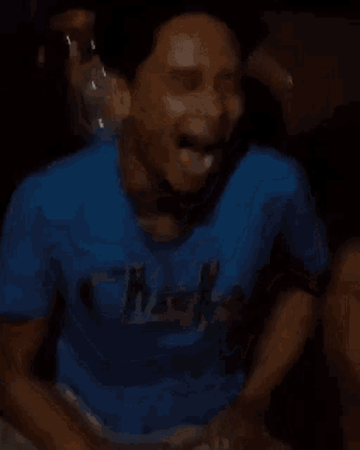 a man in a blue shirt is laughing with his mouth open in the dark .