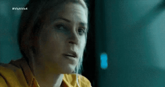 a woman in a yellow shirt is sitting in a dark room and looking at the camera .