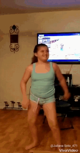 a girl in a blue tank top and shorts is dancing in a living room