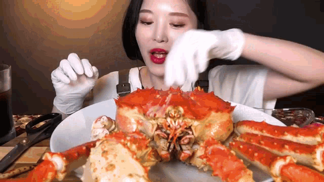 a woman wearing white gloves is eating a crab on a plate