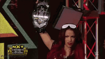 a woman is holding a trophy in front of a screen that says nxt