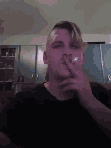 a man is smoking a cigarette in a kitchen while looking at the camera .