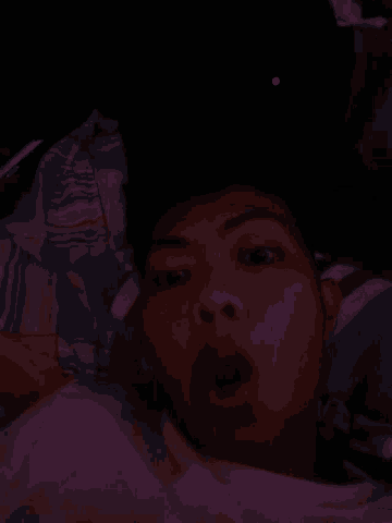 a man is laying on a bed with his mouth open and his eyes closed in the dark .