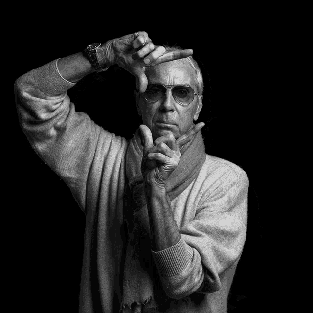 a man wearing glasses and a scarf makes a frame with his hands