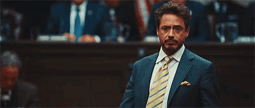 a man in a suit and tie is giving a peace sign while standing in front of a crowd .