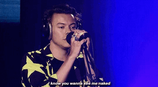 harry styles is wearing headphones while singing into a microphone on stage .