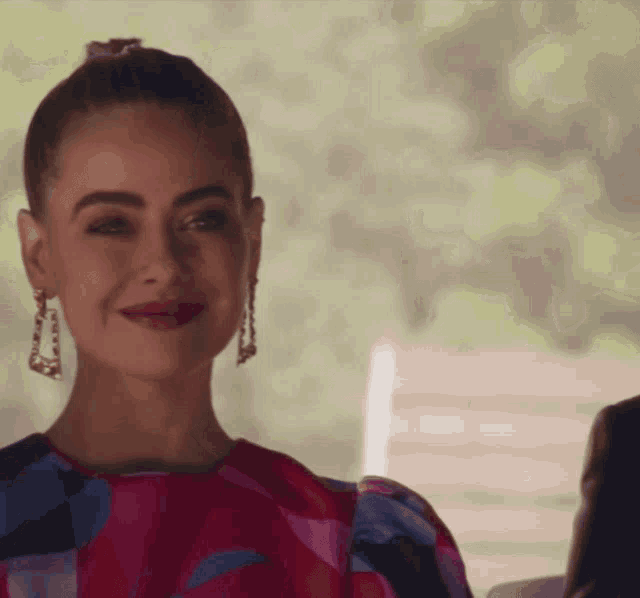 a woman wearing a colorful dress and earrings smiles at the camera