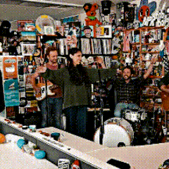 a group of people are standing in a room with a drum set and a woman singing