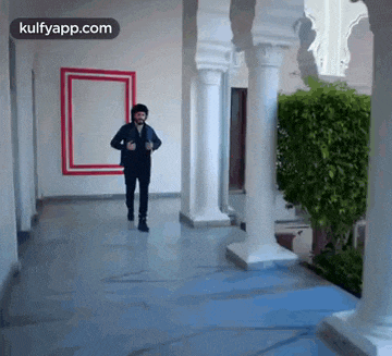 a man is running in a hallway with columns and a red and white frame on the wall .