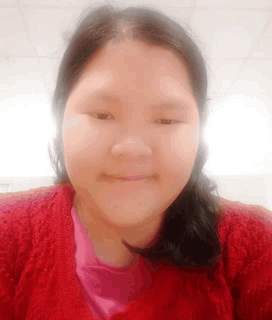 a woman wearing a red sweater and a pink shirt is smiling .