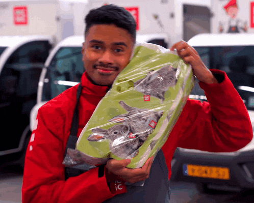 a man in a red jacket is holding a green bag with a picture of a cat on it
