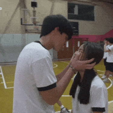 a man kisses a girl on the forehead in a gym with the letter d on the bottom right