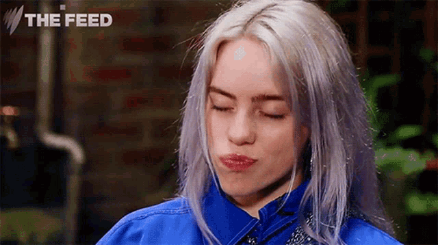 billie eilish is wearing a blue jacket with her eyes closed .