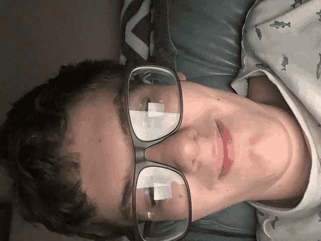 a young man wearing glasses is smiling and laying on a couch