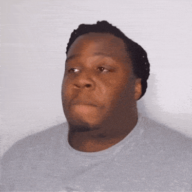 a man with dreadlocks is wearing a gray shirt and making a funny face .
