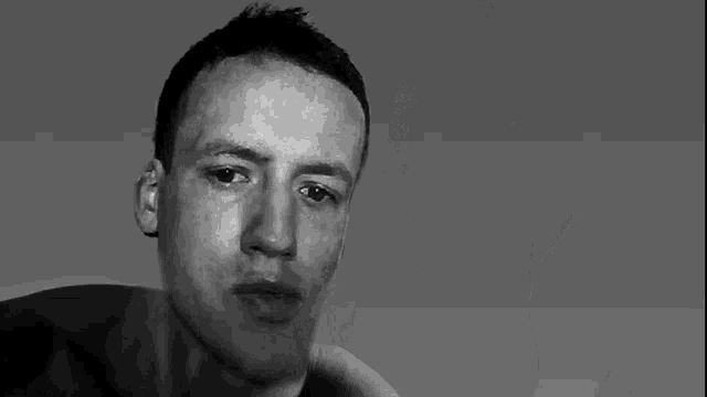 a black and white photo of a shirtless man looking at the camera .