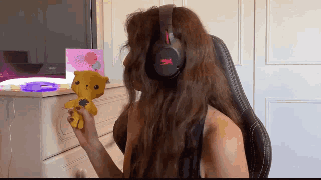 a woman wearing headphones is holding a stuffed animal in front of a sony tv