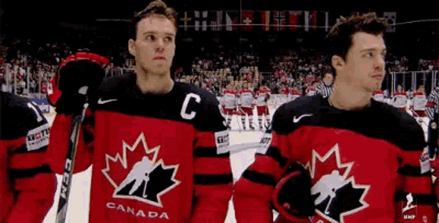 a group of canadian hockey players are standing on the ice in front of a crowd .