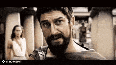 a man with a beard is standing in front of a woman and looking at the camera .