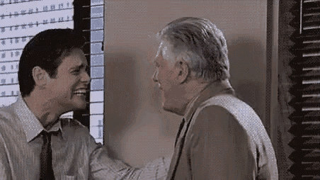 two men are laughing and hugging each other in front of a computer monitor .