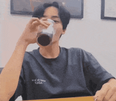 a man wearing a viga t-shirt is drinking a glass of soda