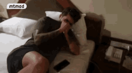 a man is laying on a bed covering his face with his hand .