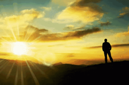 a man stands on top of a hill at sunset with the sun shining through the clouds