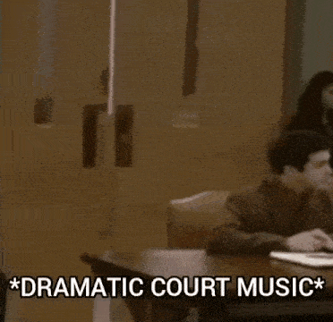 a man in a suit and tie is standing next to a man sitting at a table with dramatic court music written on it .