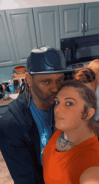a man wearing a hat with a smiley face on it kisses a woman on the cheek
