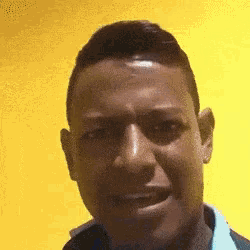 a man in a blue shirt is smiling in front of a yellow background