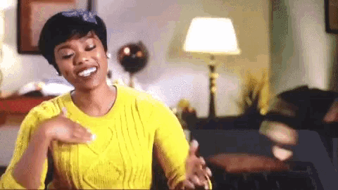 a woman in a yellow sweater is sitting on a couch in a living room and smiling .