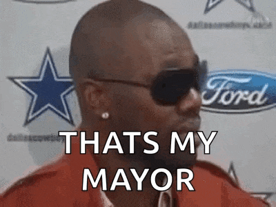 a man wearing sunglasses and a red shirt is standing in front of a ford logo .