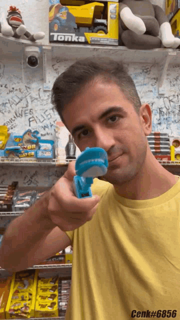 a man in a yellow shirt is holding a blue toy in front of a toy truck that says tonka