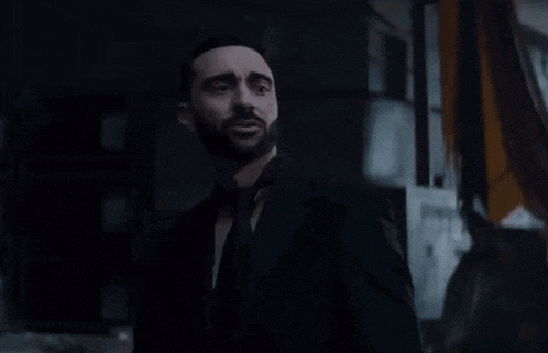 a man with a beard is wearing a black suit and tie
