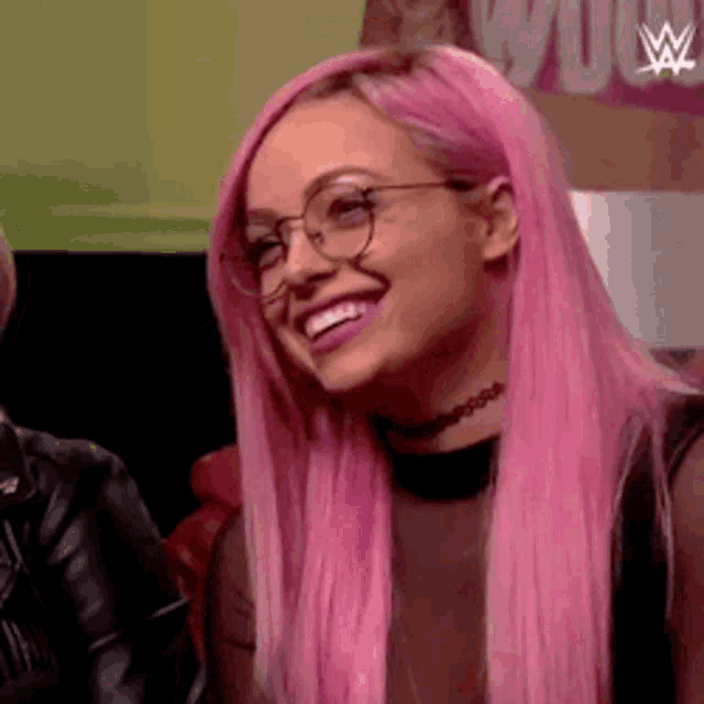 a woman with pink hair and glasses is smiling and wearing a choker necklace .
